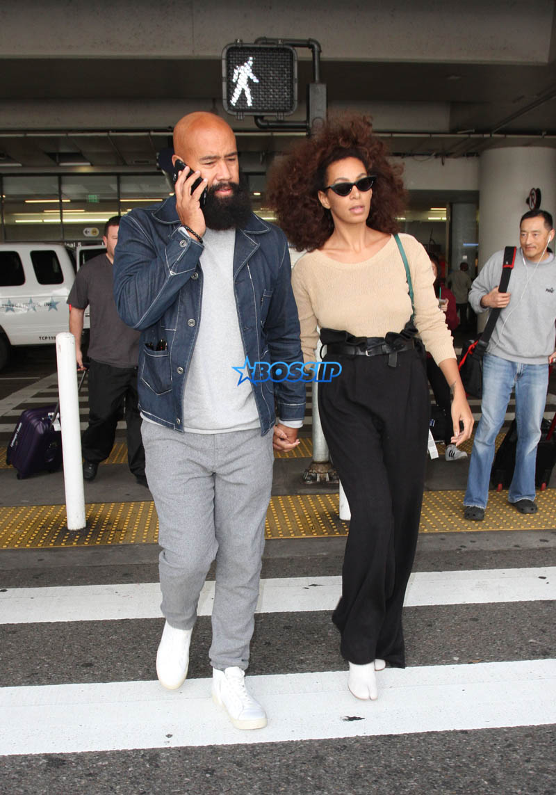 Solange Knowles husband, Alan Ferguson at LAX with highwater pants, camel-toe shoes and a beige top. SplashNews beard denim jacket white sneakers holding hands