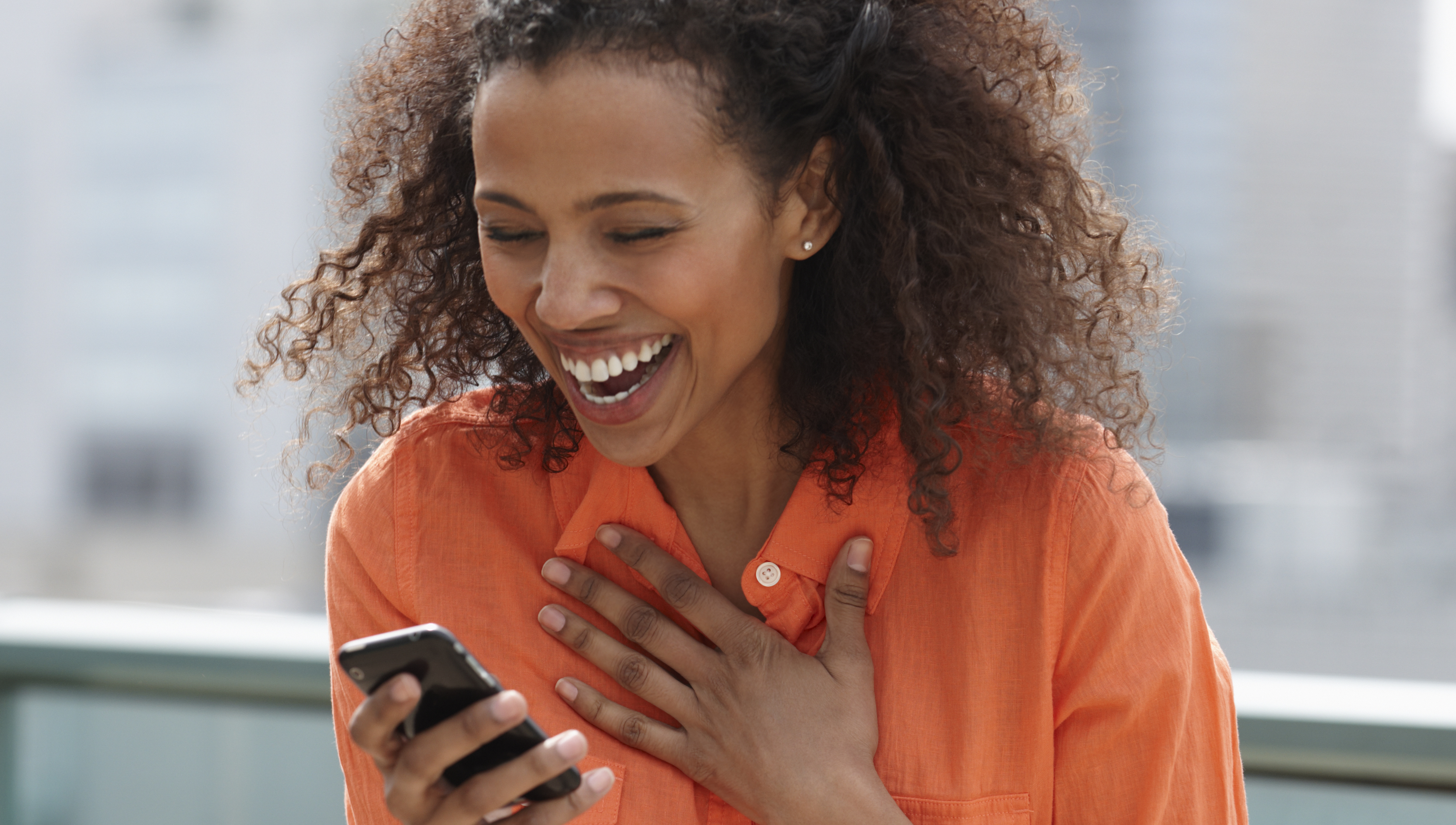 Laughing Black woman text messaging on cell phone