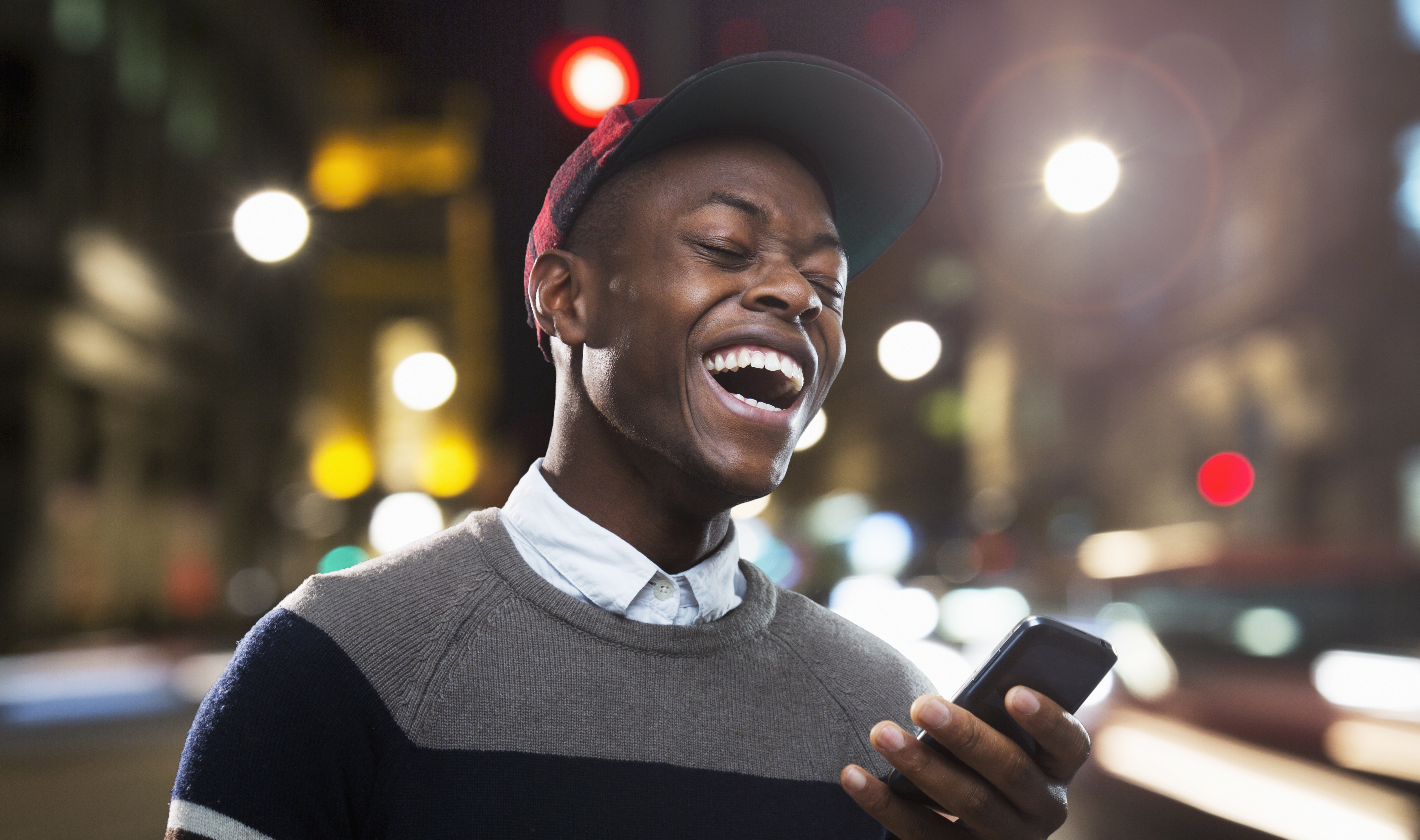 Man laughing at phone in urban street at night