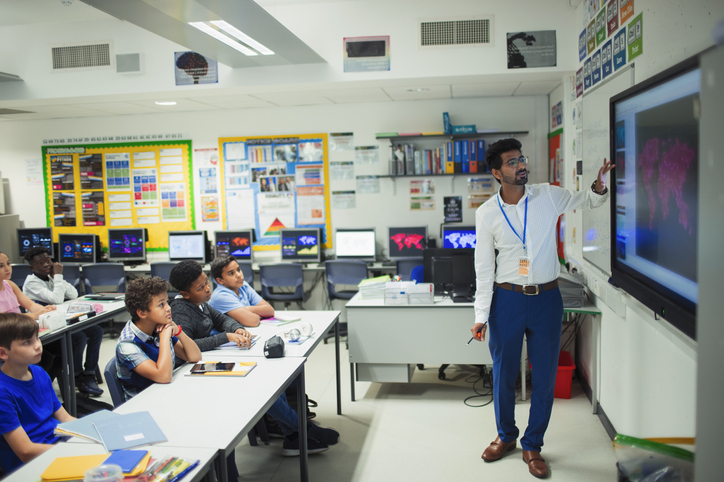 Male teacher leading lesson at touch screen in classroom