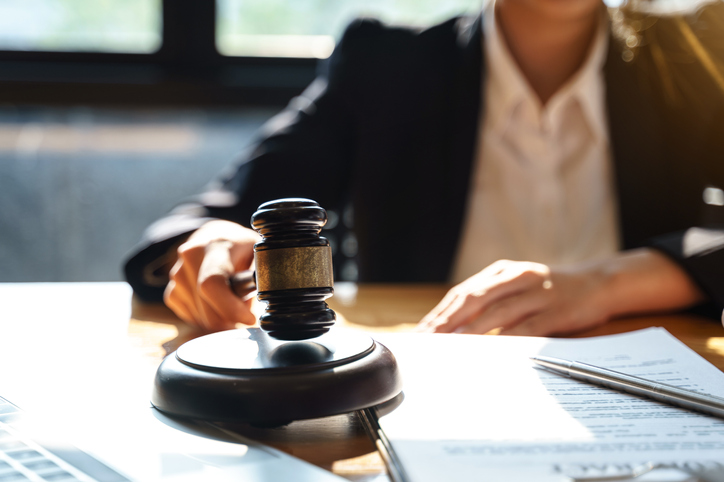 Midsection Of Lawyer Holding Gavel At Desk In Courtroom