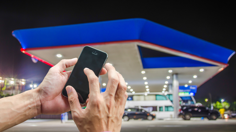 Cropped Hand Of Person Using Mobile Phone Against Gas Station At Night