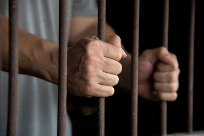 Close-Up Of Man Holding Prison Bars