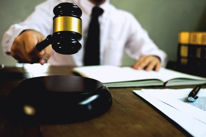 Midsection Of Lawyer Banging Gavel At Desk In Courtroom