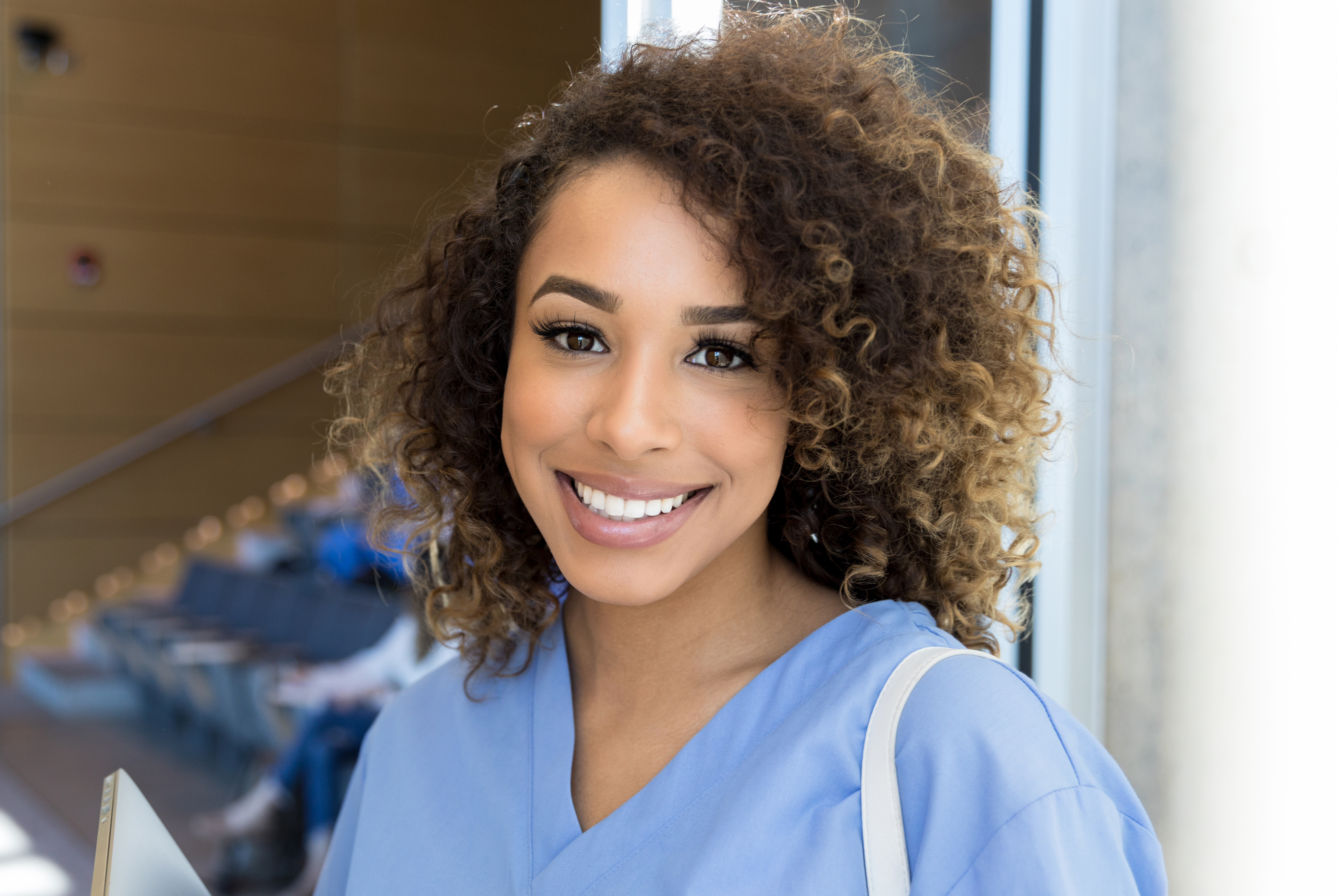Smiling nursing student in scrubs leaves lecture hall - stock photo