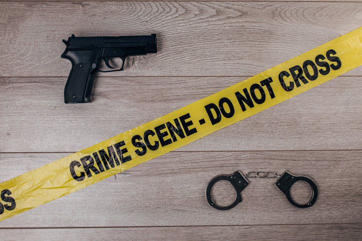 Crime scene tape, handcuffs and gun on wooden background