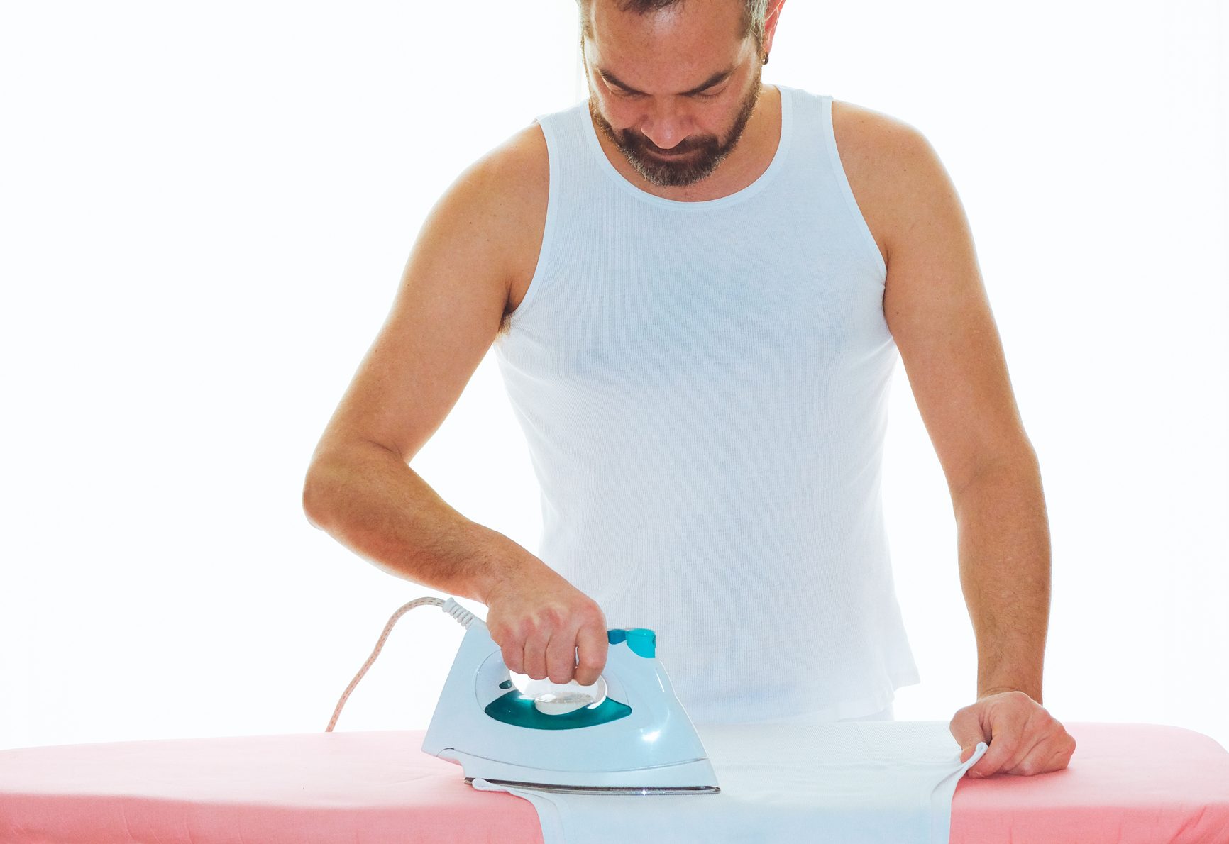 Man ironing undershirt against white