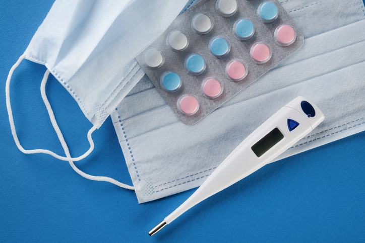 Protective Medical Disposable Masks, Thermometer, Tablets And Medications On A Blue Background. The concept of Healthcare and Medicine.