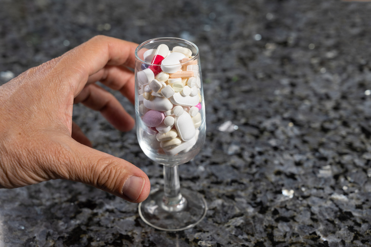 A man is going to take large amount of pills in crystal liqueur glass