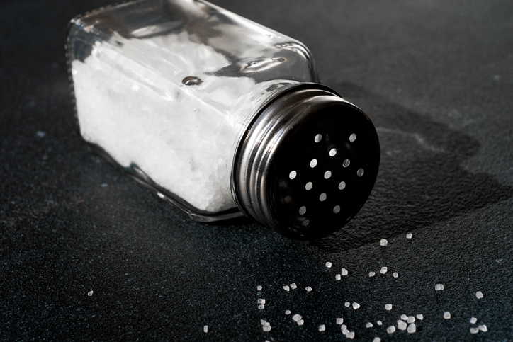 Natural, organic, sea, white salt, poured from a fallen salt shaker, on a dining table or a black background. The concept of cooking healthy food, cosmetology. A copy of the text space.