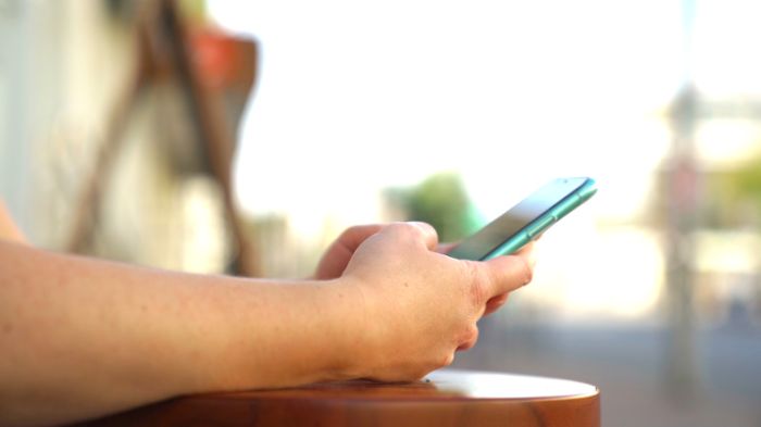 Side view of woman hands holding new smartphone on blurred city street background. Media. Close up of a girl texting or browsing on her electronic modern device outdoors.