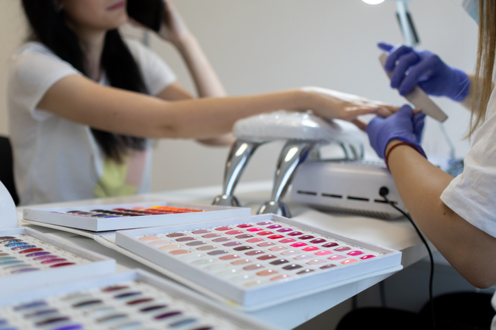 Young woman on manicure treatment in beauty salon. Professional nail care and painting in modern beauty salon. UV lamp gel polish manicure process.