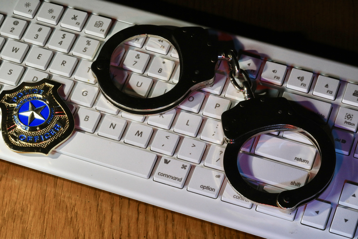 Concept of cybercrime and cybersecurity with keyboard, handcuffs, and police badge