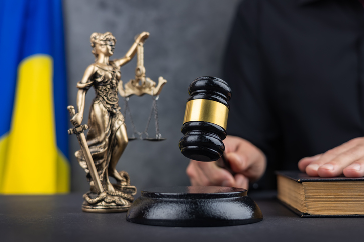 Judge with gavel and Themis Lady Justice against flag of Ukraine and dark background