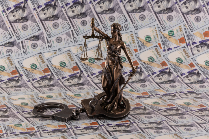 Handcuffs and the figure of Themis against the background of 100 US dollar bills